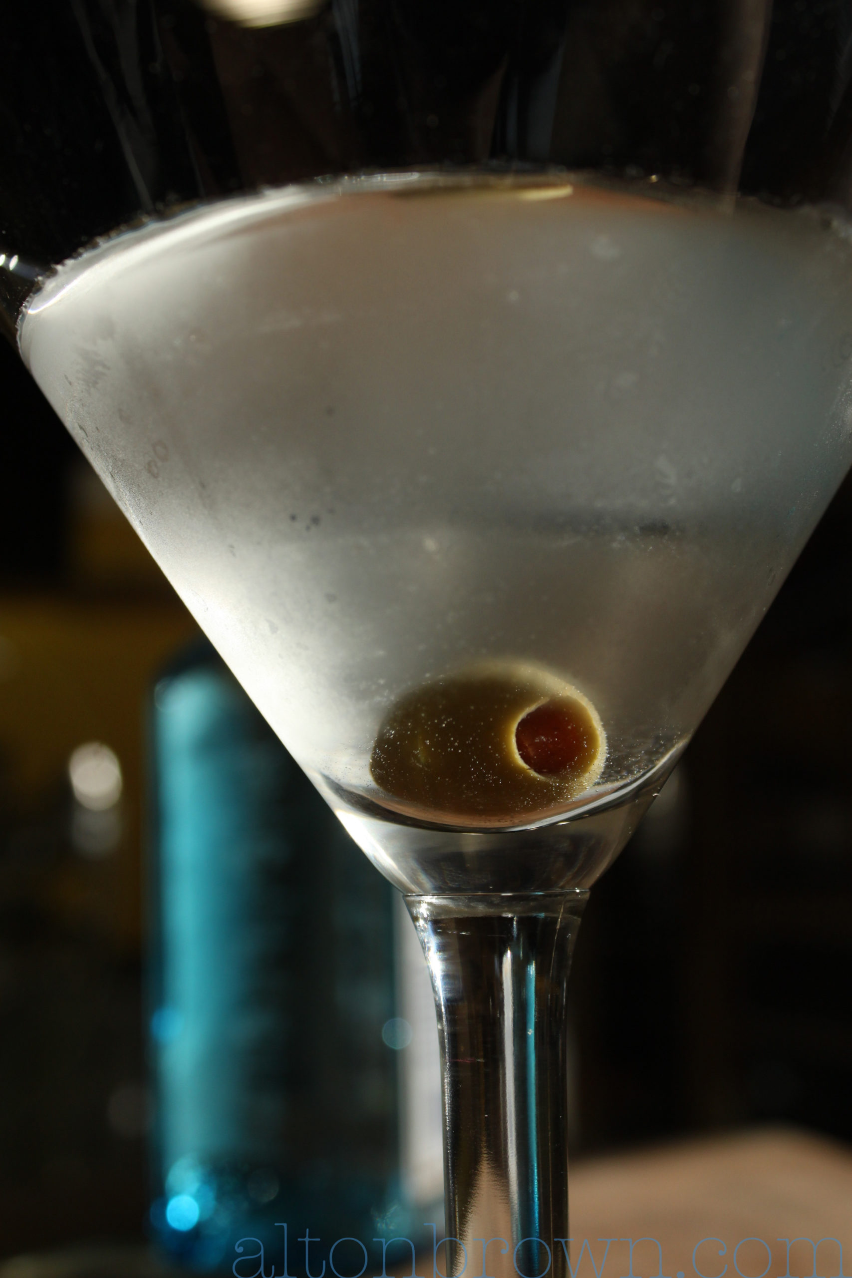 Alton Brown's classic martini in a martini glass with a green olive.