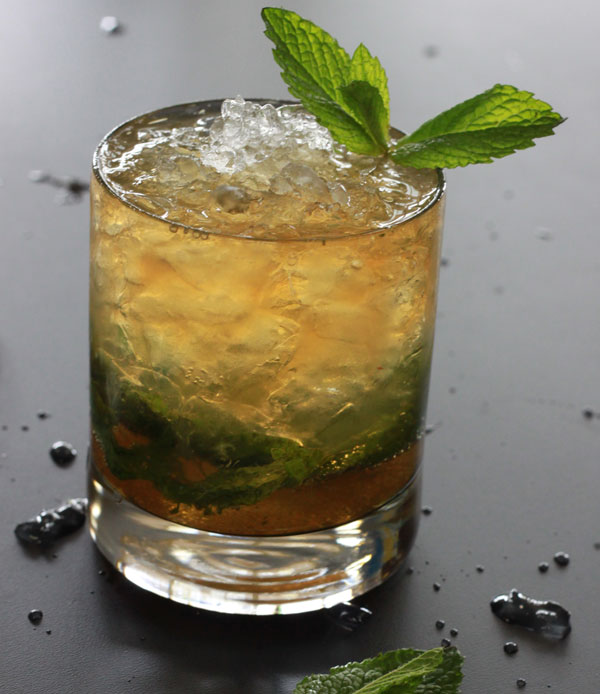 Alton Browns mint julep with crushed ice in a rocks glass and a mint sprig garnish.
