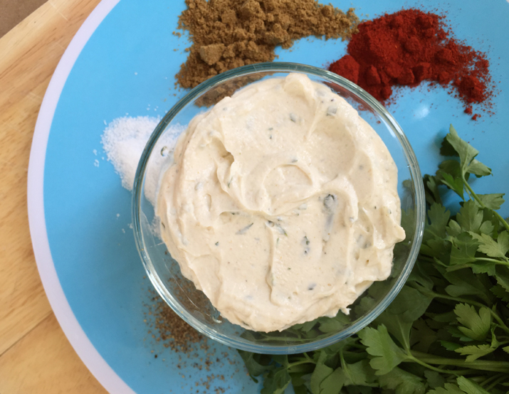 Savory Greek yogurt dip in a clear bowl set on a blue place surrounded by spices and herbs.