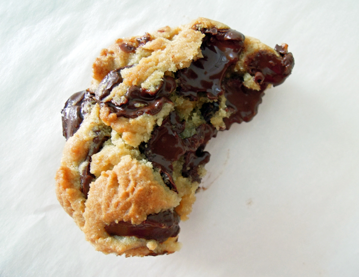 A chocolate chip cookie overflowing with lots of chocolate & broken open to show fillings.