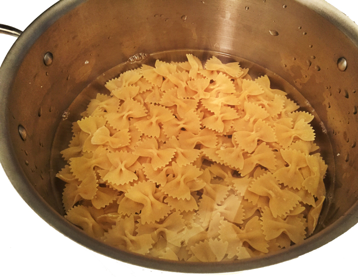 Bowtie pasta sitting in water in a large pot.