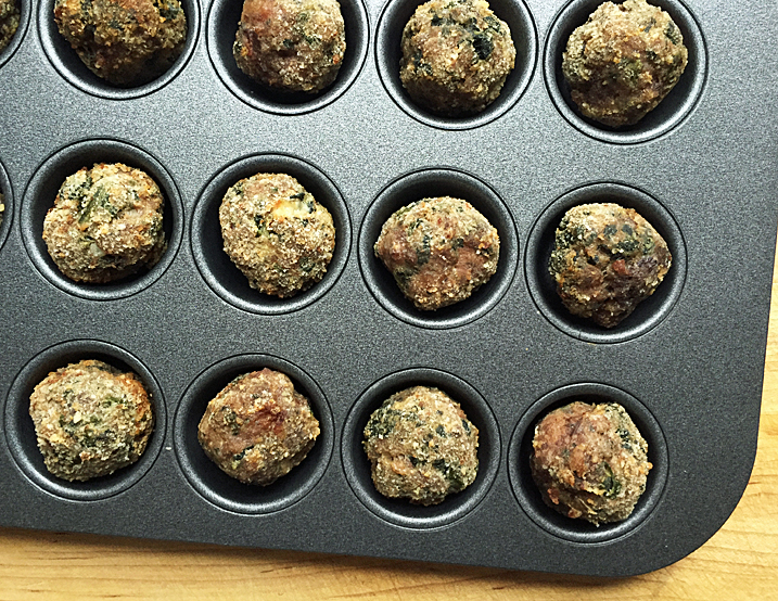 Meatballs sitting in muffin tin on wood table.