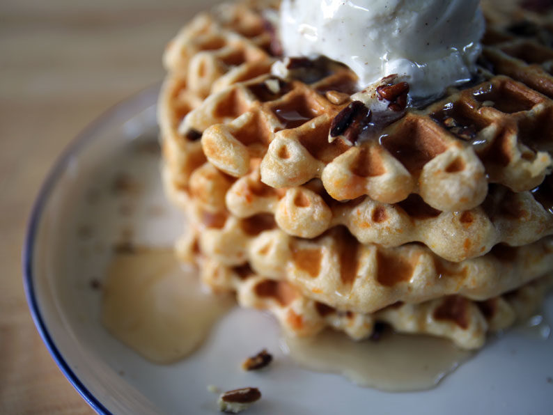 Stacked sweet potato waffles topped with pecans, syrup, and whipped cream.