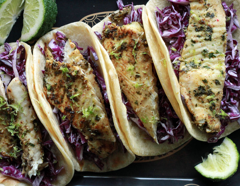 Tequila lime fish tacos with creme and red cabbage slaw lined up on a serving platter.