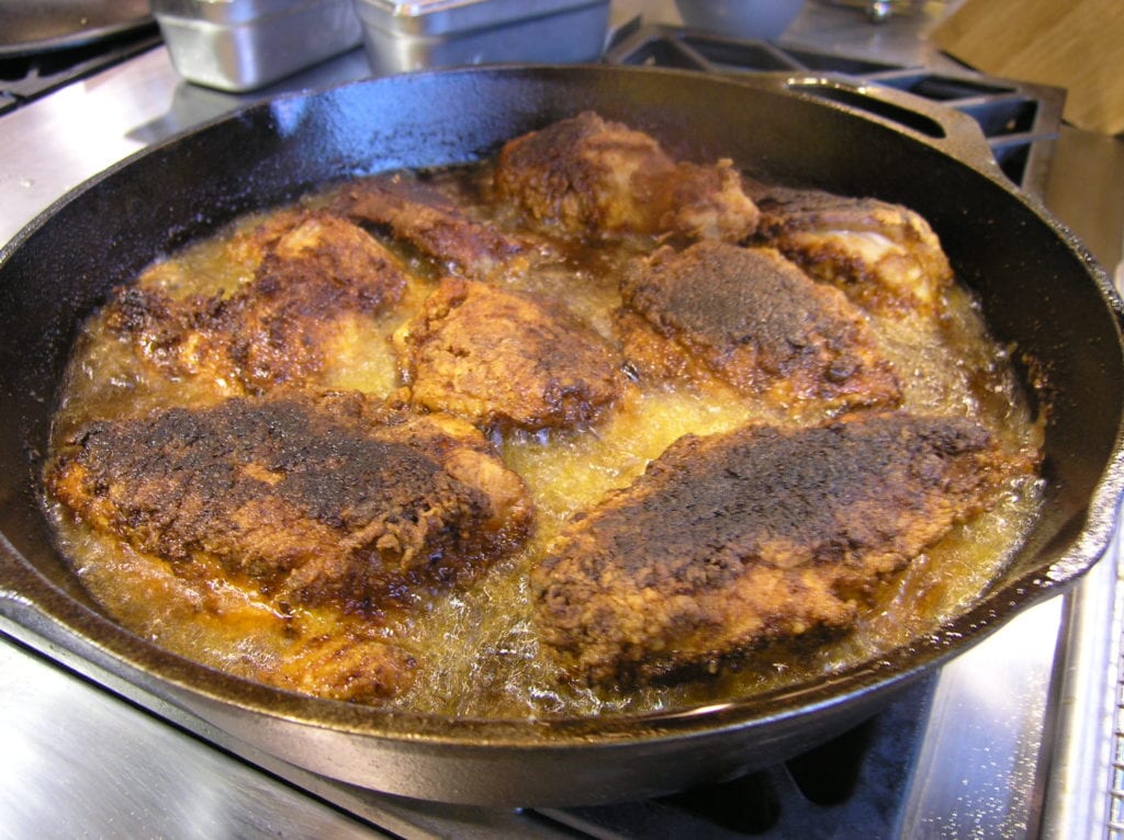 Fried chicken frying in a cast-iron skillet on the set of Alton Brown's Good Eats.