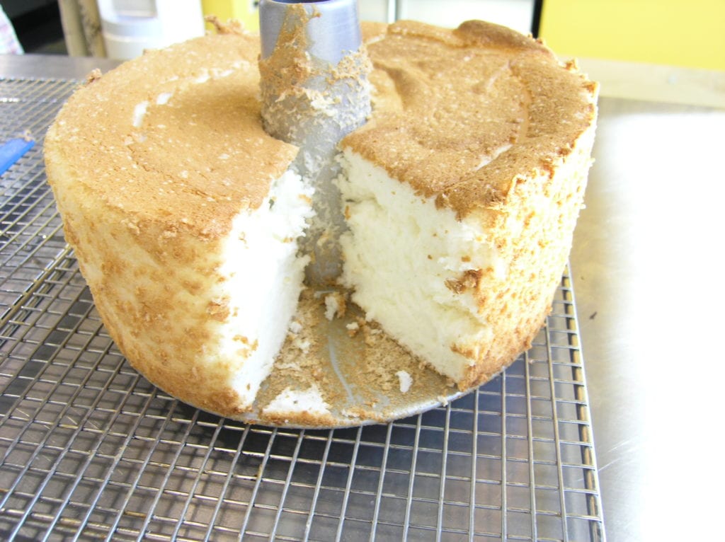 Angel food cake on a wire rack with a slice missing.