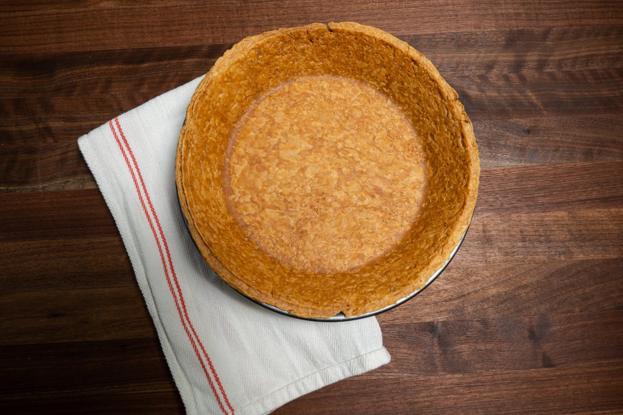 Pre-made pie crust in a pie pan on a tea towel on a wooden countertop.