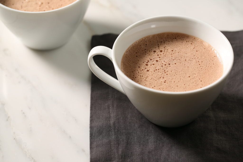 Hot cocoa in a white mug sitting on a black napkin.