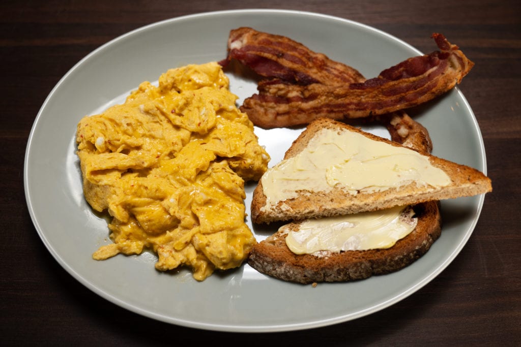20 second scrambled eggs with harissa on a grey plate with bacon and buttered toast.