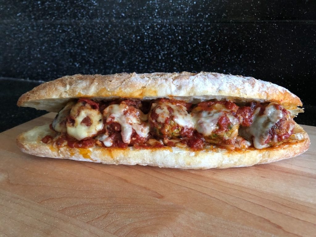 Chicken Parmesan meatballs in a meatball sub on a wooden countertop.