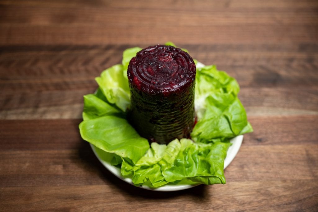 Alton Brown's congealed cranberry sauce on a white plate garnished with green lettuce leaves.