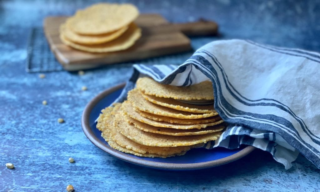 Corn tortillas stacked on a blue plate and wrapped in a kitchen towel.