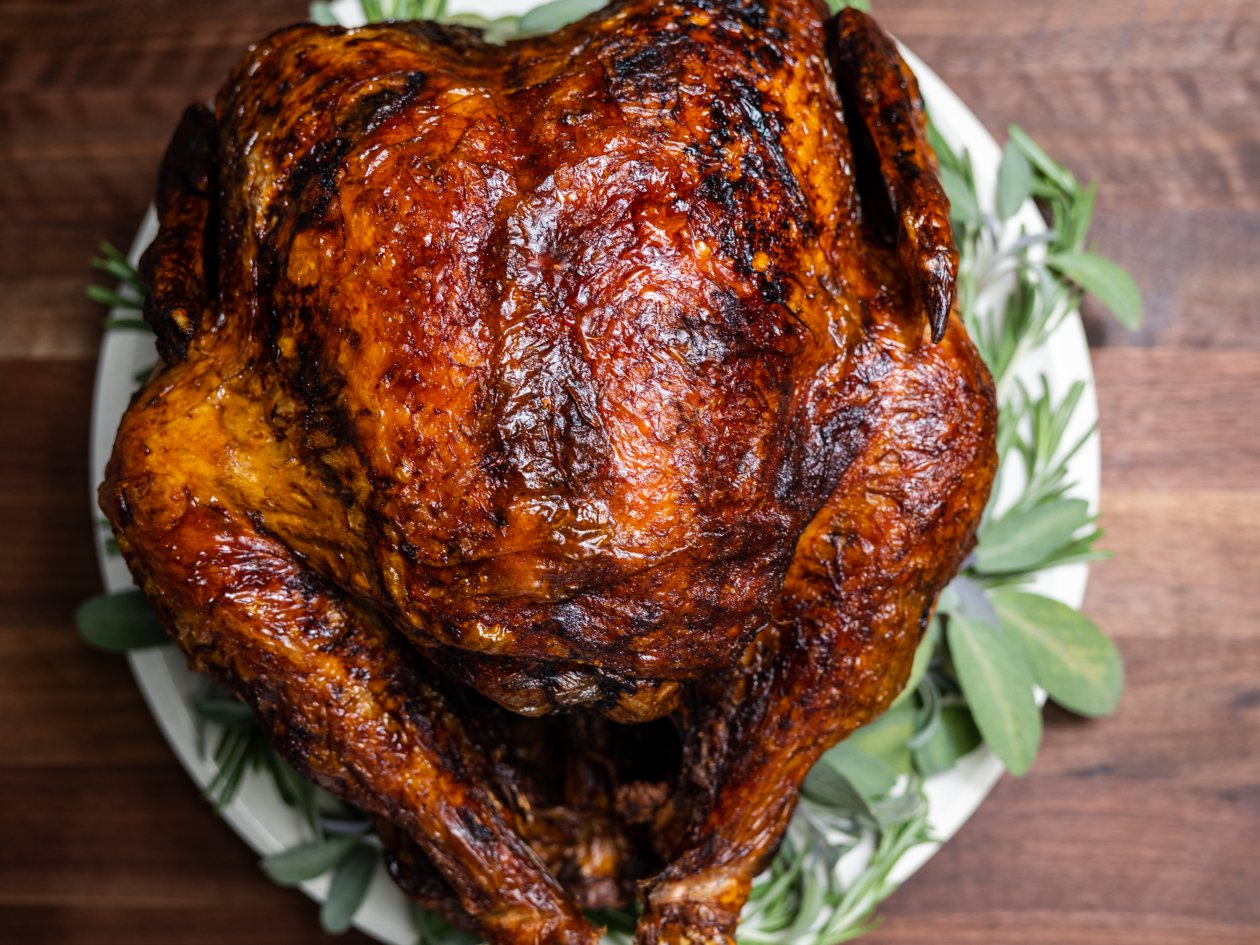 Deep-fried turkey from Alton Brown on a white platter garnished with greenery.