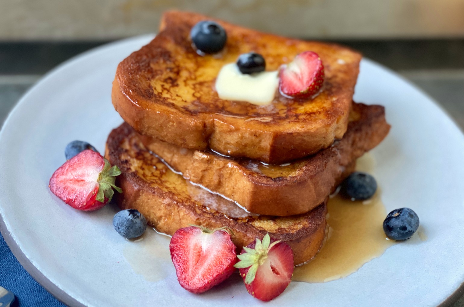 French toast slices stacked high and topped with syrup, a pat of butter, strawberries and blueberries.