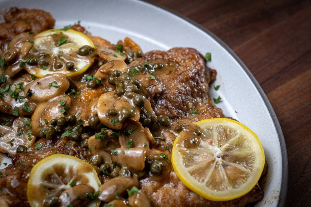 Good Eats chicken piccata on a white platter garnished with lemon slices.