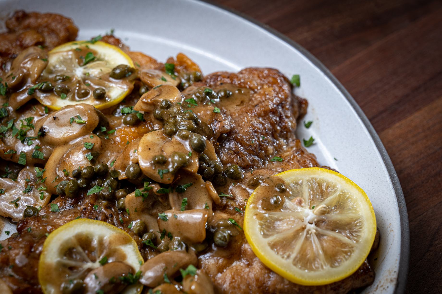Good Eats chicken piccata on a white platter garnished with lemon slices.