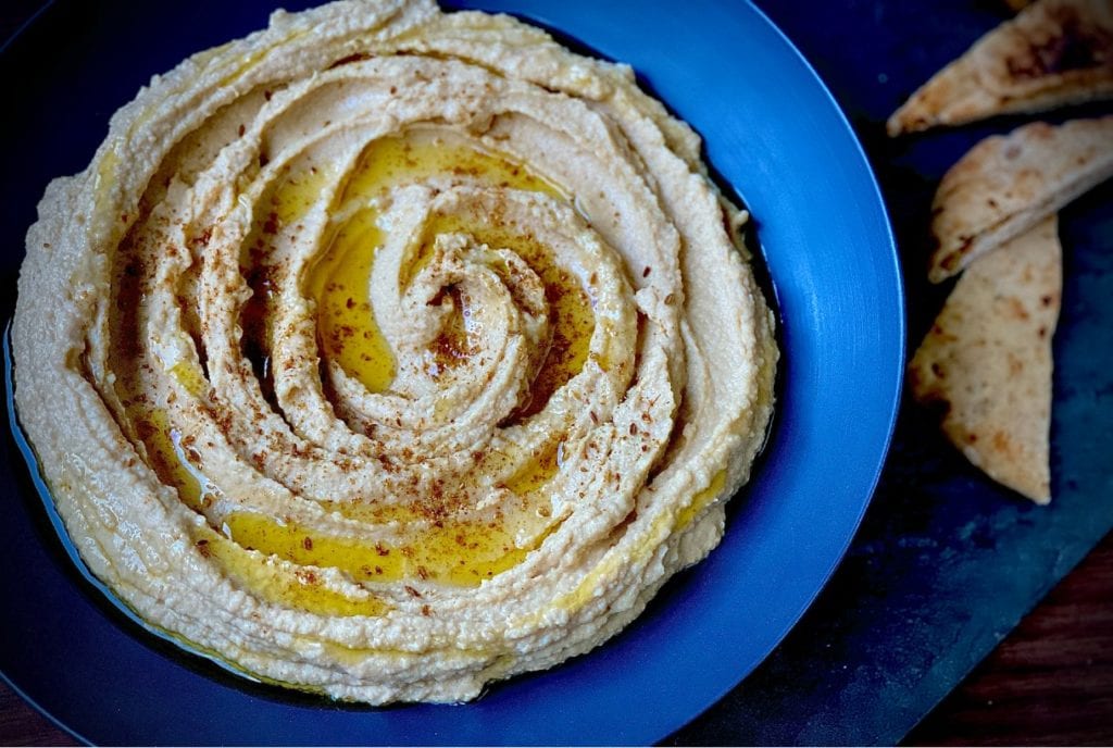 Easy homemade hummus in a blue bowl drizzled with olive oil.