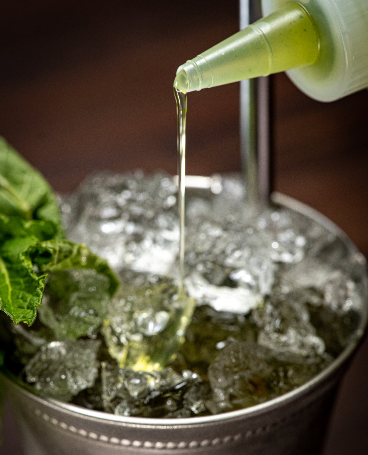 Simple mint syrup in a squeeze bottle drizzled into a mint julep cup filled with crushed ice and garnished with a mint sprig.