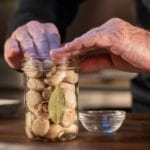 Alton Brown packing pickled mushrooms and bay leaves into a glass canning jar.