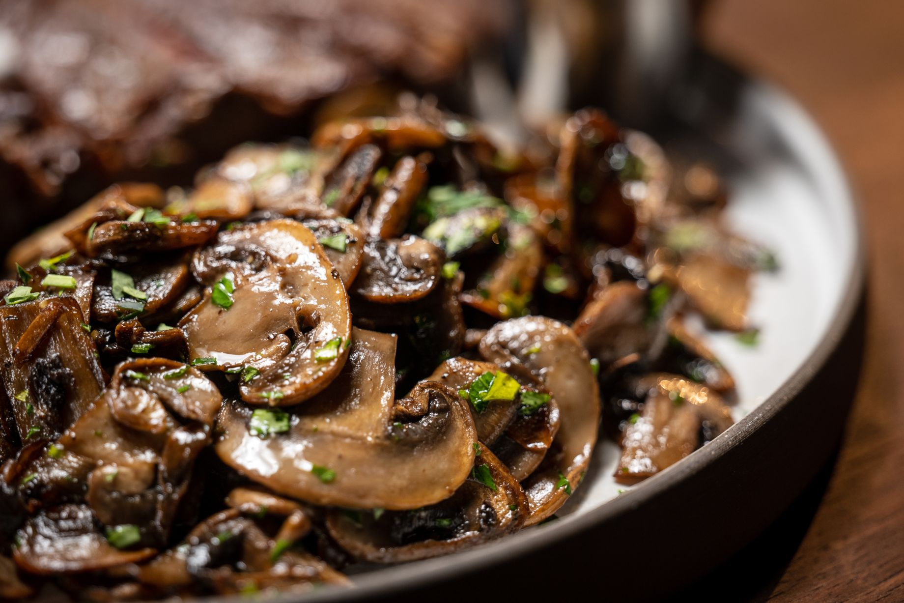 Sauteed mushrooms in a black bowl garnished with parsley.