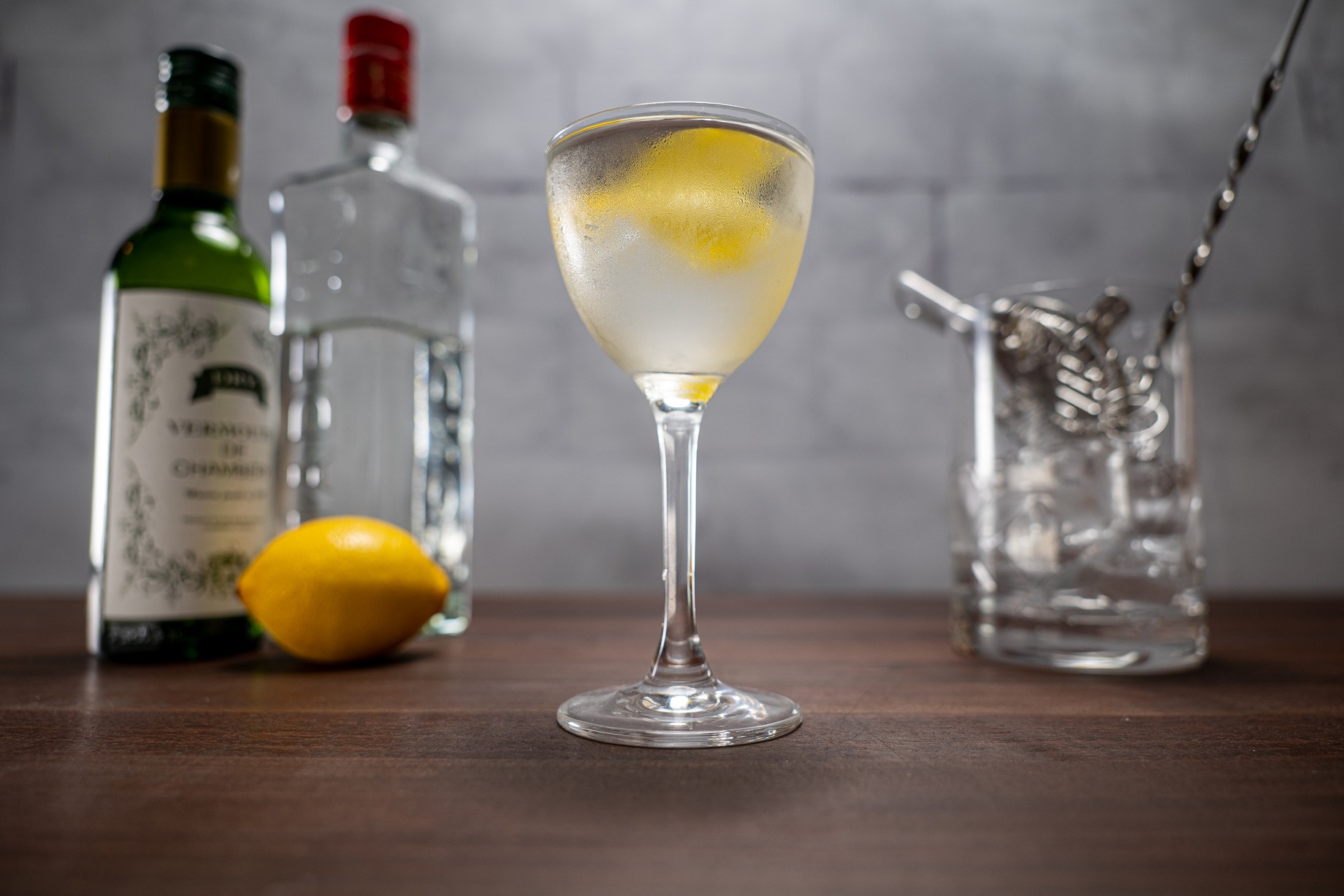 Alton Brown martini garnished with a twist of lemon and flanked by gin, vermouth, a lemon and a cocktail mixing glass.