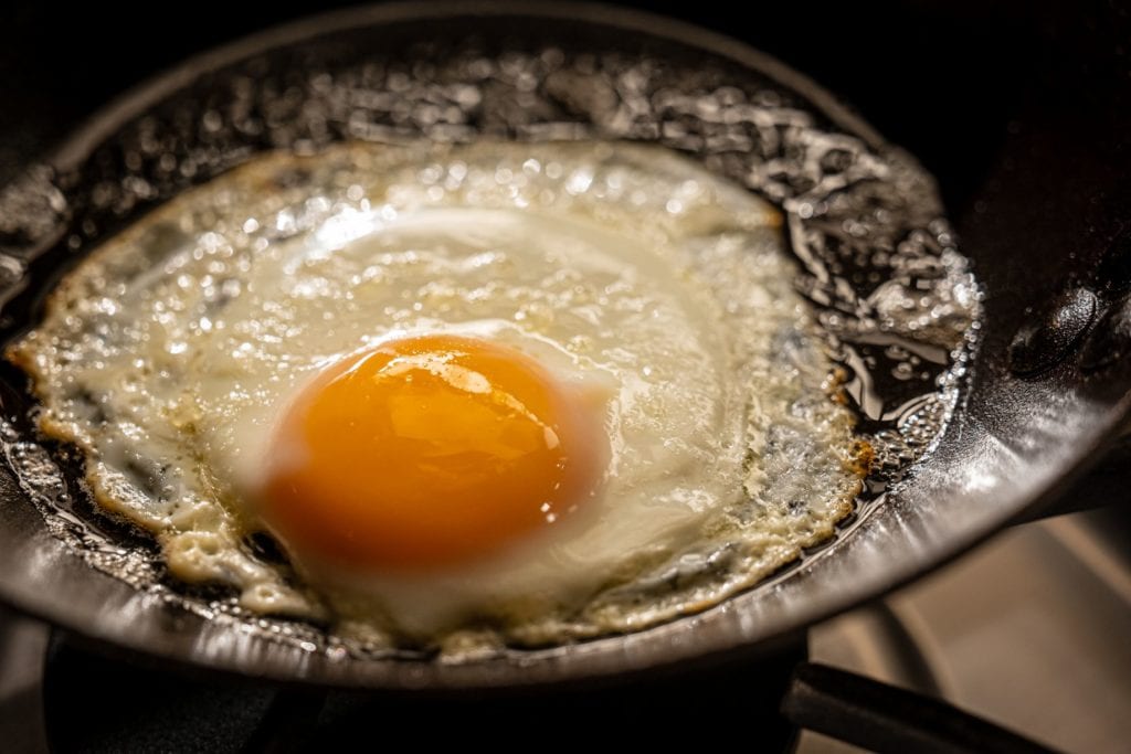 Perfect fried eggs sizzling in a cast-iron skillet on the set of Alton Brown's Good Eats Reloaded.
