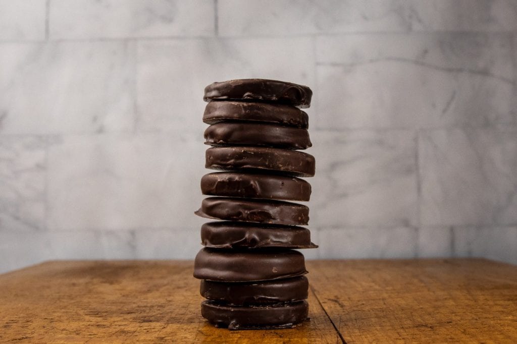 Homemade peppermint patties stacked in a tower on a wood cutting board.