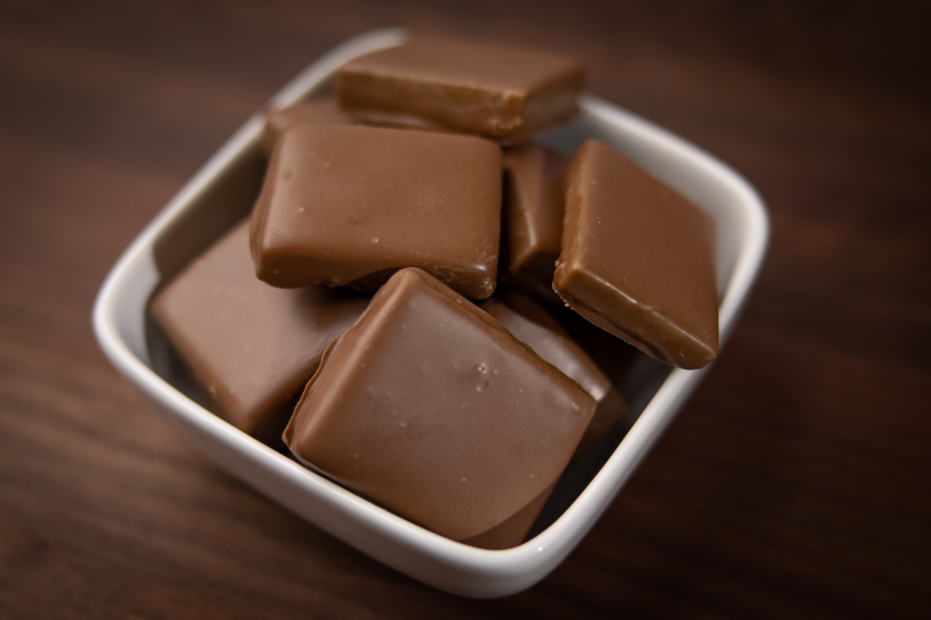 Chocolate-covered pistachio butterfingers in a white, square bowl.