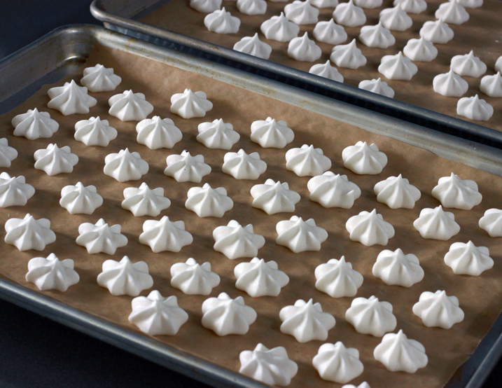 Aquafaba meringues piped into star shapes on two parchment paper-lined half-sheet pans.
