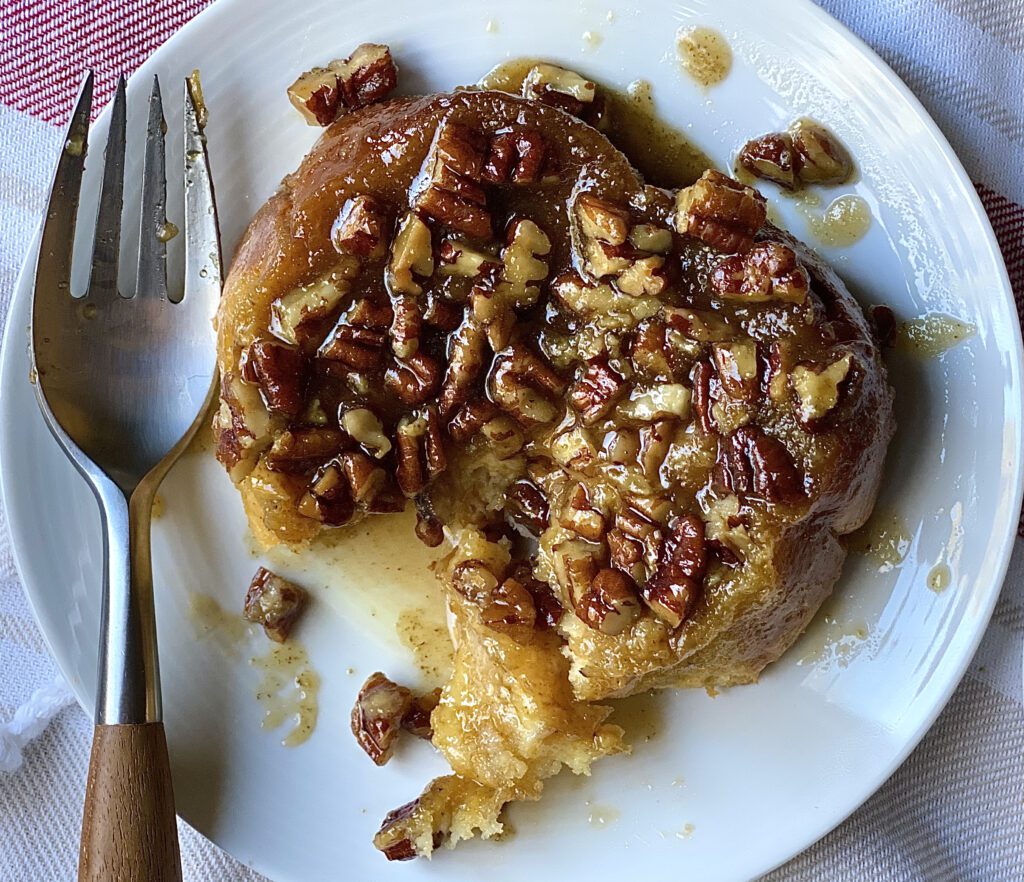 Golden-brown Pecan Sticky Bun French Toast served on a white plate, drizzled with caramel sauce and topped with crunchy pecans.